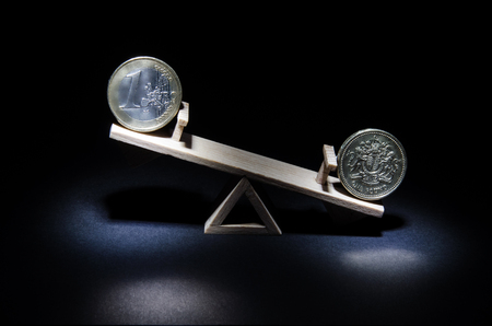 Coins of the euro and a pound on a wooden swing symbolizing the change of the course. Objects on a black matte background.の写真素材