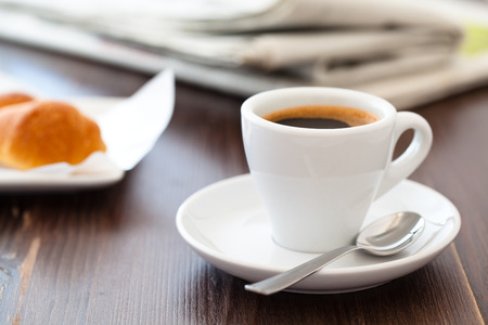 Cup of coffee on wooden table with stacked newspapers in background.の写真素材