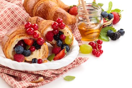 Fresh croissants with fruits. Isolated on white background. Focus on jar of honey and on fruits on the top of croissants.の写真素材