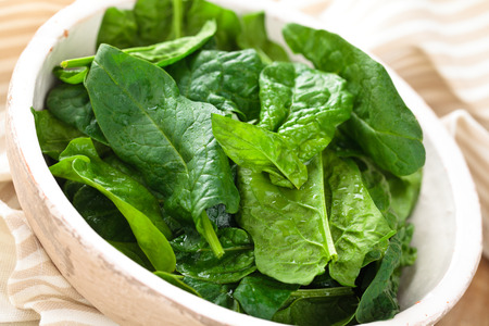 Spinach leaves in plate on rustic wooden table.