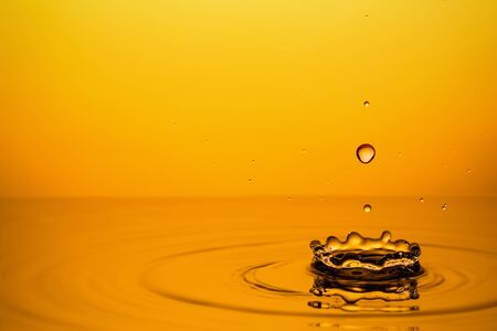 Ripple of the golden surface of yellow liquid with crown and drops.の写真素材