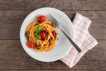 Spaghetti with tomato sauce and basil in a white bowl on a dark wooden surface.の写真素材