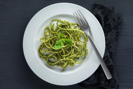 Spaghetti pasta with pesto sauce, basil, pine nuts and parmesan top view.