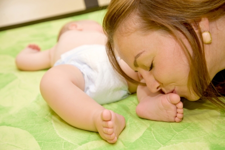 Pretty young mother kissing the tiny feet of her newborn baby who is sleeping in bedの写真素材