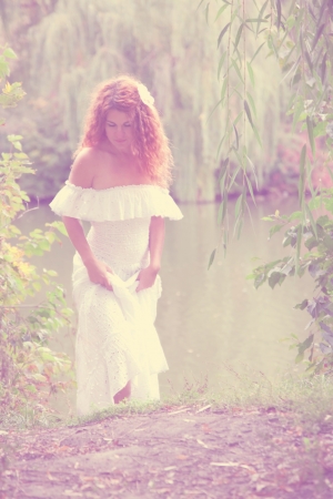 Vintage photo - beautiful young red-haired woman in white dress with flower in her hair or bride or undine, coming out of the river in thickets of willow. Retro styleの写真素材