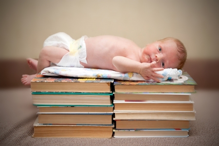 Tiny naked newborn baby lying on a pile of booksの写真素材