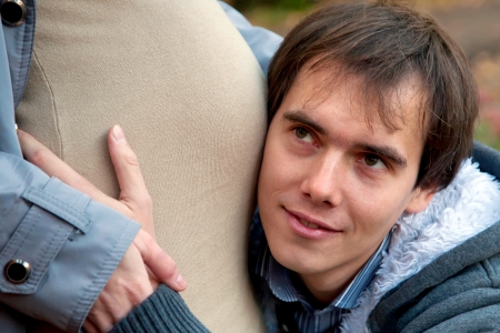 Happy young future father listening to his wife s pregnant bellyの写真素材