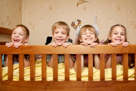 Four children, two brothers and two sisters lying on the bed, looking over a side and laughing. Happy family. Triplet and their older sister.の写真素材