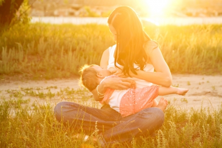 Mother breast feeding  baby in the sunlight at sunset. Summer holiday.の写真素材
