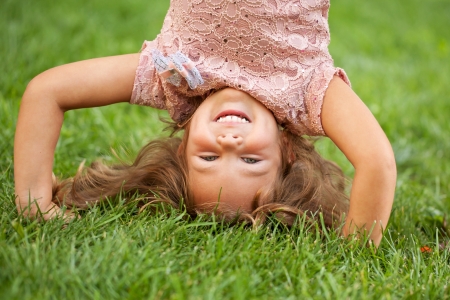 Funny happy little girl standing on her head on the grass in the park.