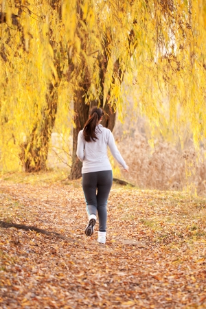 Middle-aged woman running on the trail in a forest or park. Rear view. Healthy lifestyle concept.の写真素材