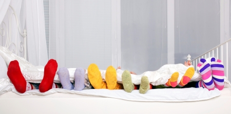 Happy family concept. Feet of father, mother and four children in colorful knitted socks on white bed. Family sleeping together.の写真素材