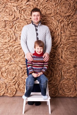 Father and son. Son sitting on a stool, his father standing behind him and hugging him.の写真素材