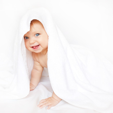 Baby playing hide and seek under the towel and showing tongue.の写真素材