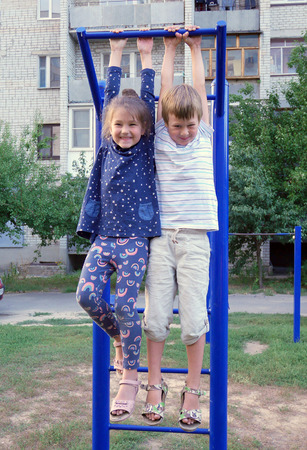 Boy and girl playing in the yard on the playground. Children are hanging on the bar.
