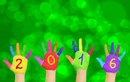 Kids colorful hands forming number 2016 against New Year blurred bokeh green background.の写真素材