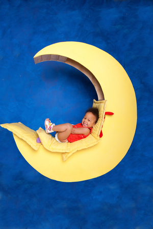 Happy black baby girl sitting on the moon against a background of blue sky.の写真素材