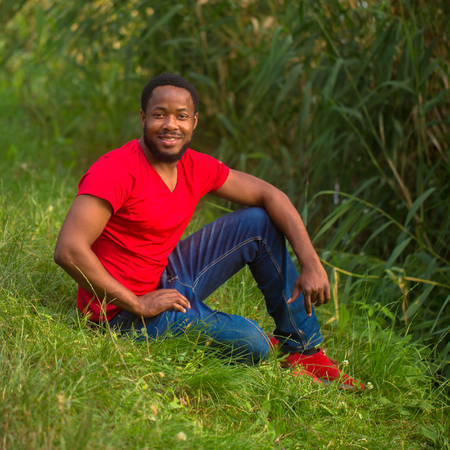 Smiling black african man resting on the green grass in the park.の写真素材