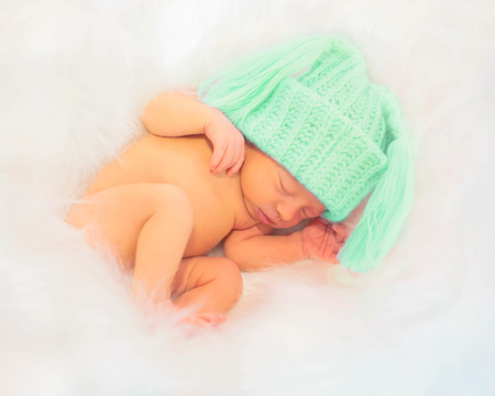 Wonderful newborn baby sleeps in a green cap on soft fur.の写真素材