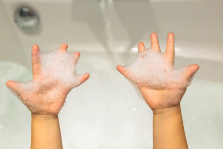 Baby hands with soap suds. Small child in the bathroom washes his hands with soap and water. Hygiene and purity since childhood. The kid likes to play with foam.の写真素材