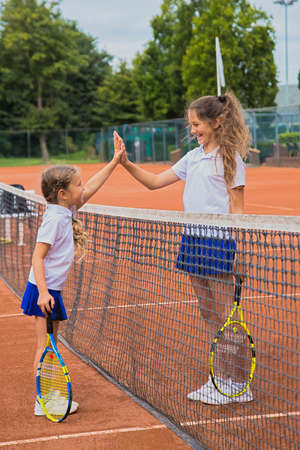 Tennis kids. Children dressed in tennis clothes on the court. Children give five each other. Sisters girls play tennis together.の写真素材