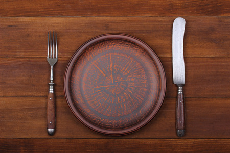 Fork, knife and dinner plate  on a brown wood backgroundの写真素材