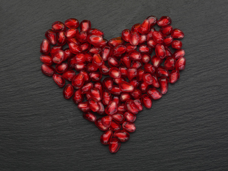 Red heart made of pomegranate grains on black stone background. Closeupの写真素材