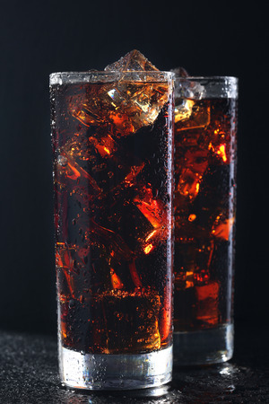 Glasses of cola with ice cubes on black stone covered by water dropsの写真素材