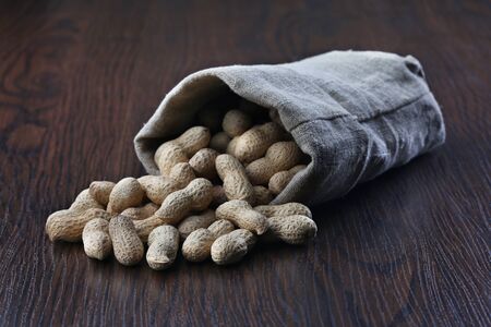 Peanuts in burlap sack on brown wooden background
