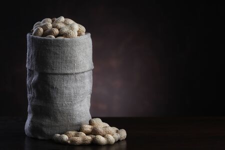 Peanuts in burlap sack on brown wooden background
