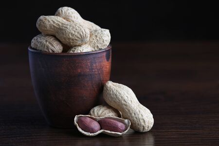 Peanuts in ceramic pot on wooden background. Closeup