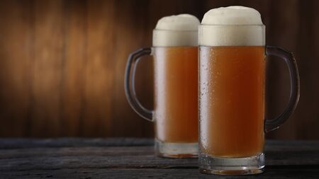 Two frosty mugs of beer on brown wooden backgroundの写真素材