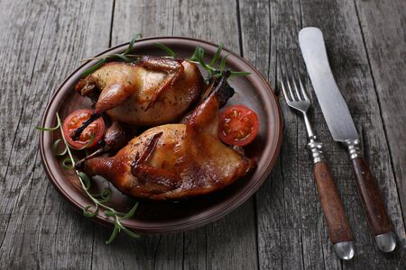 Grilled quails with rosemary and tomato on wooden backgroundの写真素材