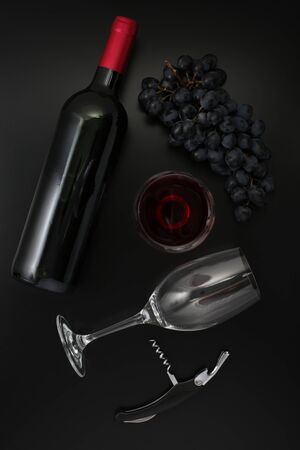 Bottle of red wine, glass, corkscrew  and ripe grapes on black background. Top view
の写真素材