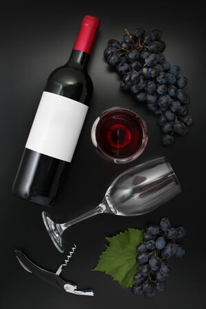 Bottle of red wine with label, glass and ripe grapes on black. Top viewの写真素材