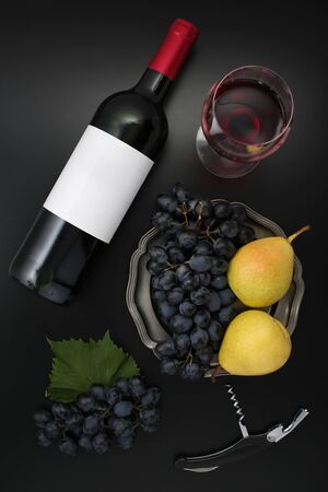 Bottle of red wine with label, corkscrew, pears  and ripe grapes on black. Top viewの写真素材