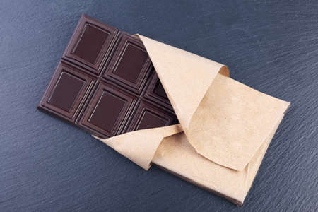 Dark chocolate bar in paper wrapper on black slate stoneの写真素材