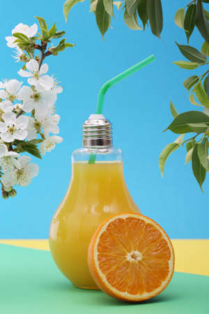 Orange juice in light bulb glass with blossom cherry branch on bright colorful background