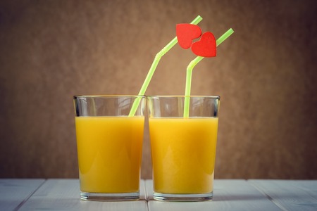 Orange juice glasses with red hearts as a kissing lipsの写真素材