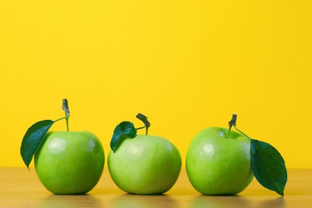 Green fresh apples with leaf against yellow backgroundの写真素材