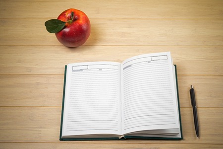 Red apple and open notebook with pan on wooden backgroundの写真素材