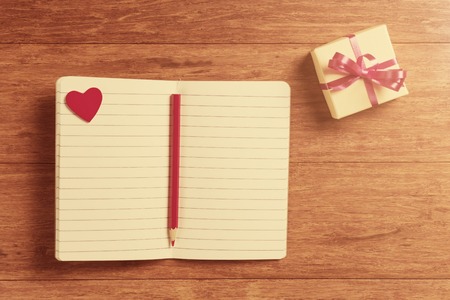 Open notebooks with red hearts and gift box on wooden backgroundの写真素材