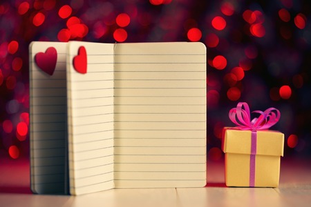Open notebooks with red hearts and gift box against defocused lights.の写真素材