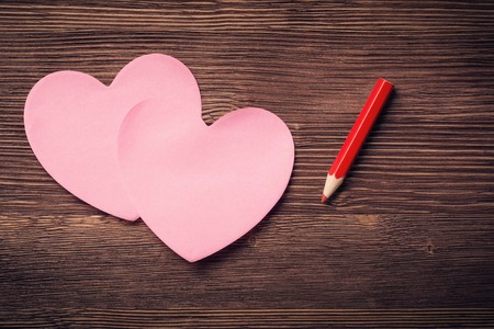Sticky notes in the form of hearts and red pencil on vintage wooden backgroundの写真素材