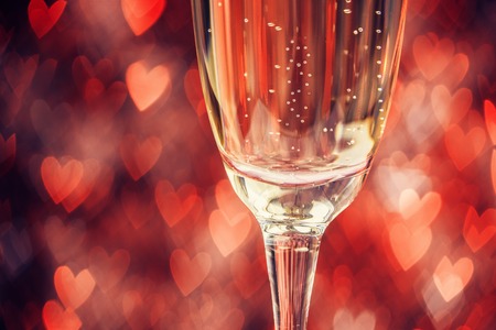 Close up of glass with champagne over abstract defocused lights shaped like heartsの写真素材