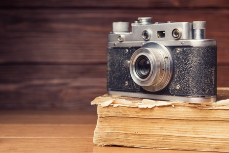 Vintage 35mm film camera on old book over wooden defocused backgroundの写真素材