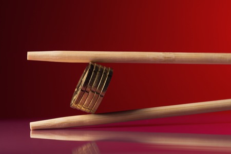 Stack of euro cent coins held by chopstick over red backgroundの写真素材