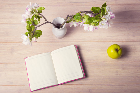 Open notebook with blossoming branch and green apple on wooden tableの写真素材