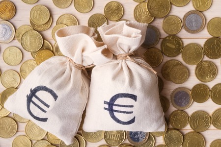 Money bags and euro coins over wooden background, focus on money bagsの写真素材