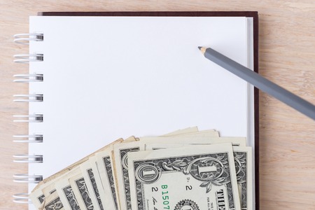Notebook with USD bills and pencil on wooden backgroundの写真素材